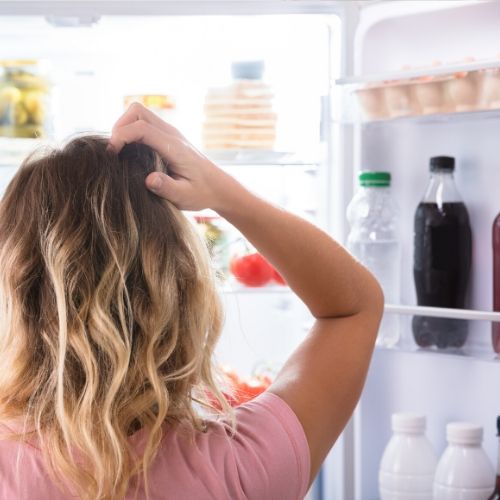woman scratchin her head looking in refrigerator needs to improvise dinner